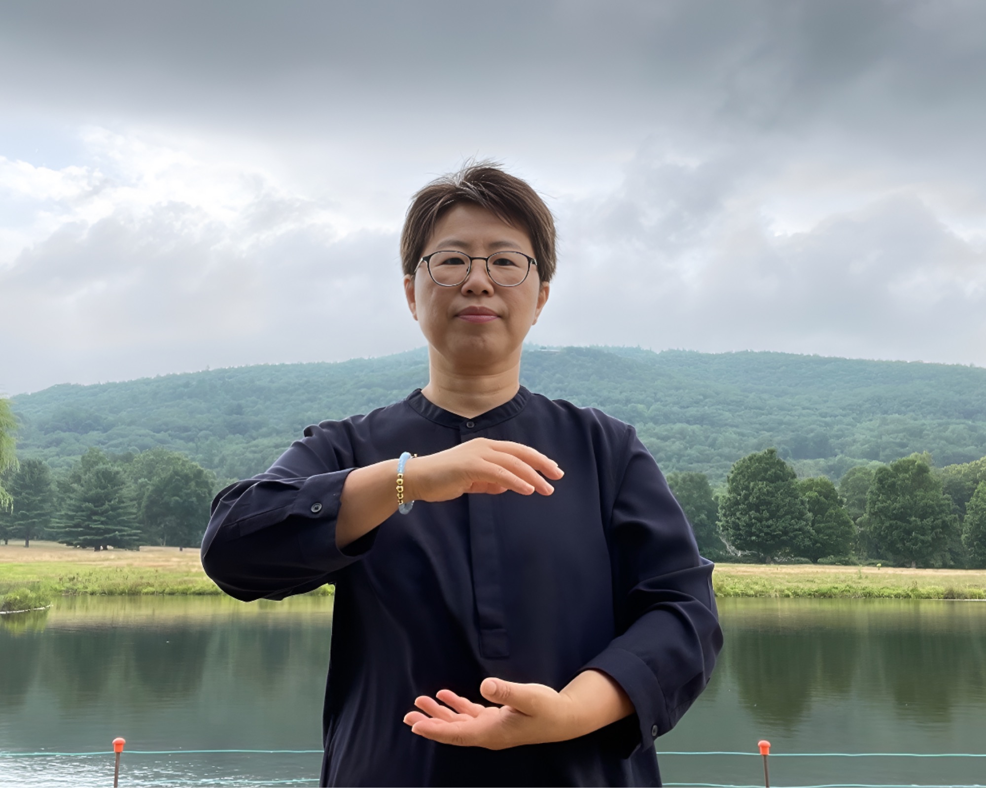 Bama Kim holding a Qigong energy-ball posture beside a lake at a retreat property